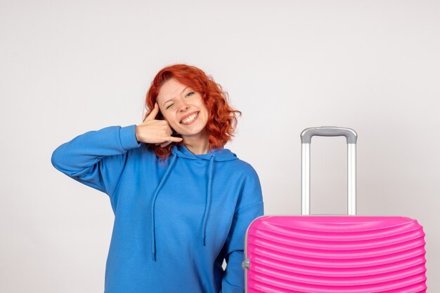 Vorderansicht des jungen weiblichen Touristen mit rosa Tasche auf weißer Wand