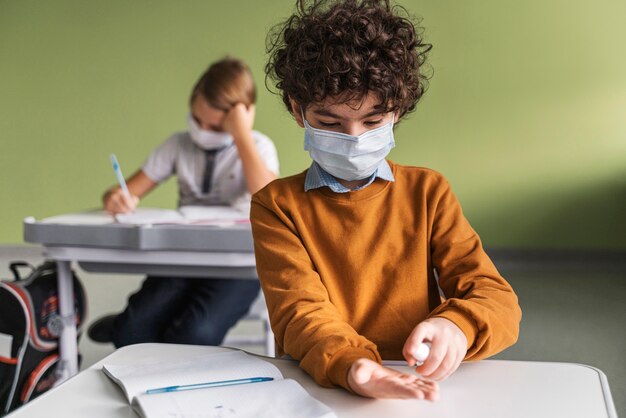 Vorderansicht des Kindes mit der medizinischen Maske, die Hände in der Klasse desinfiziert