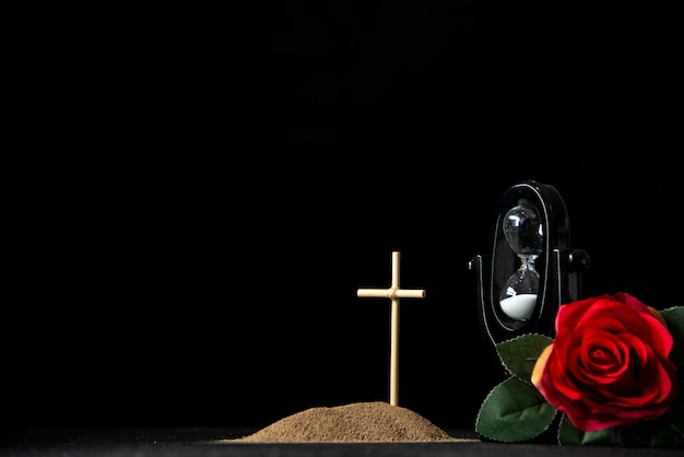 Vorderansicht des kleinen Grabes mit Sanduhr und roter Rose auf Schwarz