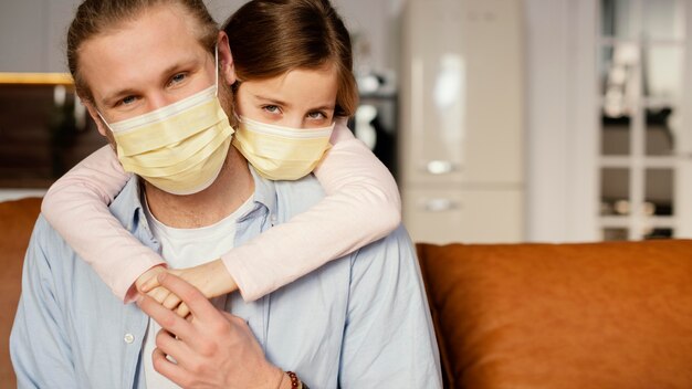 Kostenloses Foto vorderansicht des kleinen mädchens, das zeit mit vater beim tragen der medizinischen maske verbringt