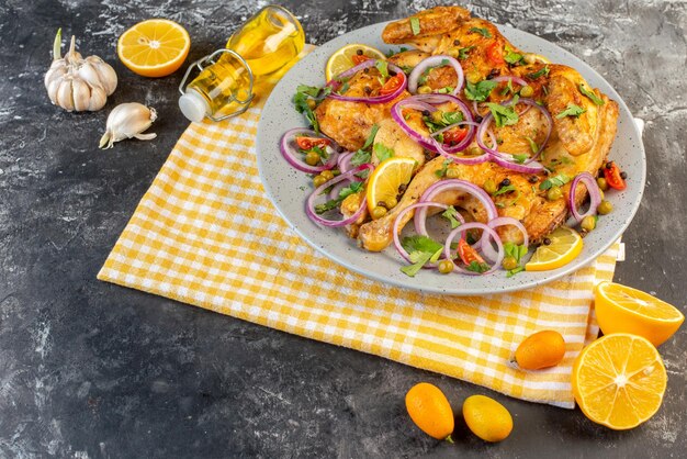 Vorderansicht des köstlichen gebratenen Hühnchengerichts mit verschiedenen Gewürzen und Lebensmitteln Knoblauch Ölflasche Zitrone auf der linken Seite auf dunklem Hintergrund