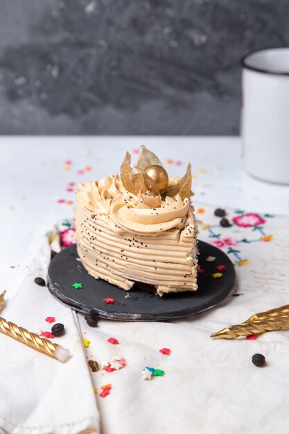 Vorderansicht des köstlichen Kuchenstücks innerhalb des dunklen Tellers mit Kerzen und kleinen Sternzeichen auf dem hellen Schreibtisch