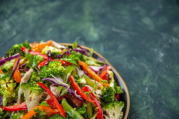Vorderansicht des köstlichen veganen Salats in einem Teller mit verschiedenem frischem Gemüse auf dunklem Hintergrund
