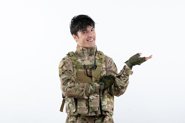 Vorderansicht des lächelnden jungen Soldaten in Militäruniform auf weißer Wand