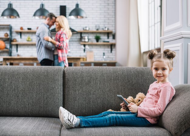 Kostenloses Foto vorderansicht des lächelnden mädchens digitale tablette mit ihren unscharfen eltern im hintergrund halten