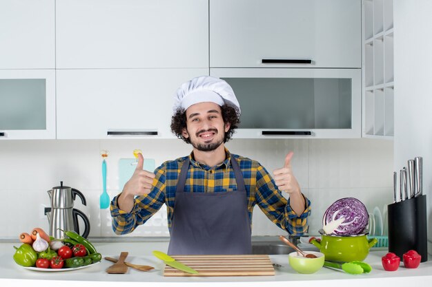 Vorderansicht des lächelnden männlichen Kochs mit frischem Gemüse und Kochen mit Küchengeräten und in der weißen Küche in Ordnung