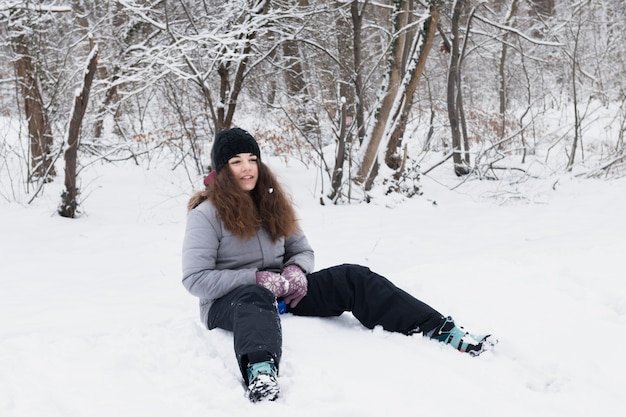 Vorderansicht des Mädchens die warme Kleidung tragend, die auf Schnee sitzt