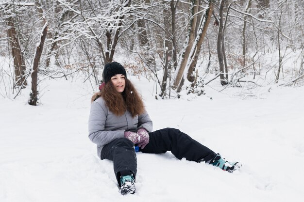 Vorderansicht des Mädchens die warme Kleidung tragend, die auf Schnee sitzt