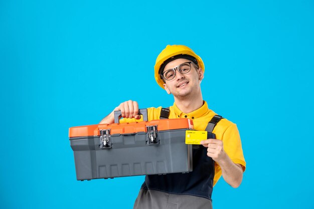 Vorderansicht des männlichen Arbeiters in der gelben Uniform, die Werkzeugkasten auf dem Blau trägt