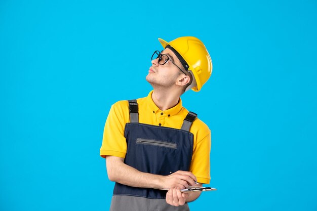 Vorderansicht des männlichen Arbeiters in der gelben Uniform mit Aktennotiz, die Notizen auf blau macht