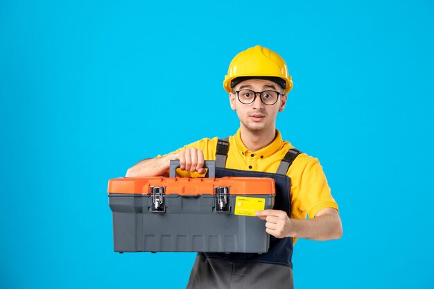 Vorderansicht des männlichen Arbeiters in der gelben Uniform mit Bankkarte und Werkzeugkasten auf Blau