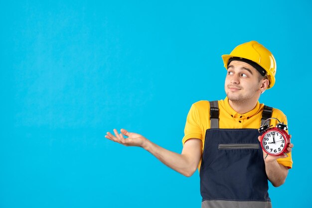 Vorderansicht des männlichen Arbeiters in der gelben Uniform mit den Uhren auf Blau