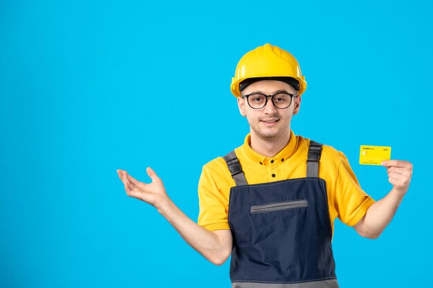 Vorderansicht des männlichen Arbeiters in der gelben Uniform mit Kreditkarte auf blau