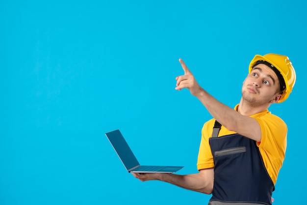 Vorderansicht des männlichen Arbeiters in der Uniform mit Laptop, der auf Blau zeigt