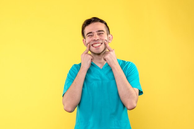 Vorderansicht des männlichen Arztes, der auf gelber Wand lächelt