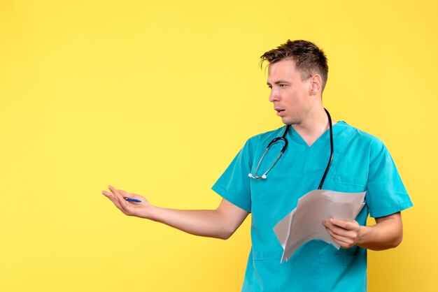 Vorderansicht des männlichen Arztes, der Dokumente auf gelber Wand hält