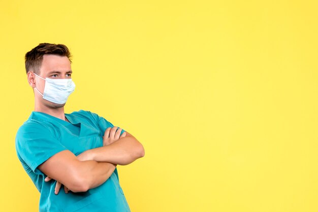 Vorderansicht des männlichen Arztes, der Maske auf gelber Wand trägt
