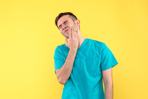 Vorderansicht des männlichen Arztes, der Zahnschmerzen auf gelber Wand hat