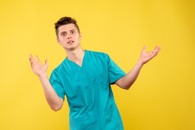Vorderansicht des männlichen Arztes im medizinischen Anzug auf gelber Wand