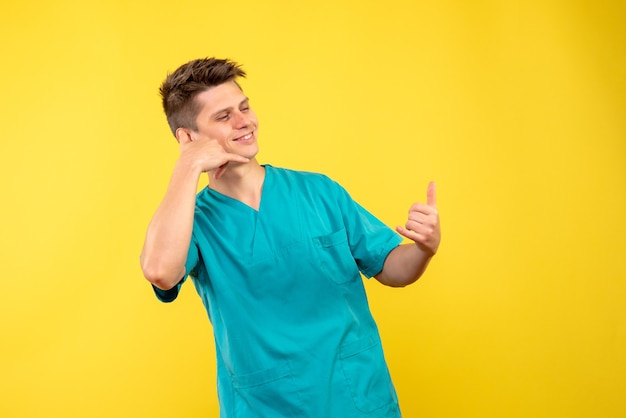 Vorderansicht des männlichen Arztes im medizinischen Anzug auf gelber Wand
