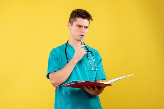Vorderansicht des männlichen Arztes im medizinischen Anzug, der Analyse auf gelber Wand hält