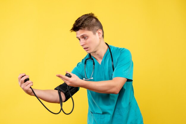 Vorderansicht des männlichen Arztes im medizinischen Anzug, der Druck auf gelbe Wand prüft