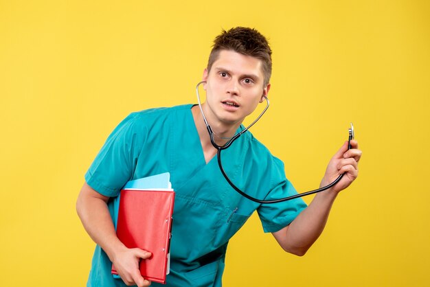 Vorderansicht des männlichen Arztes im medizinischen Anzug mit Analyse und Stethoskop auf gelber Wand