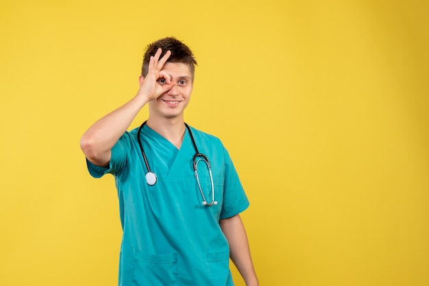 Vorderansicht des männlichen Arztes im medizinischen Anzug mit Stethoskop auf gelber Wand