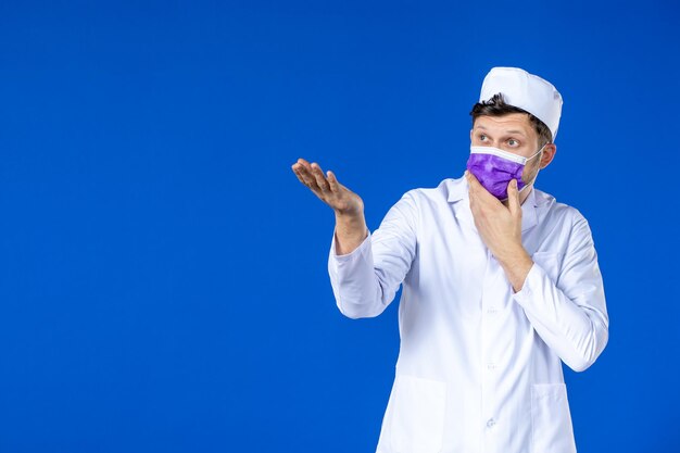 Vorderansicht des männlichen Arztes im medizinischen Anzug und in der lila Maske auf Blau