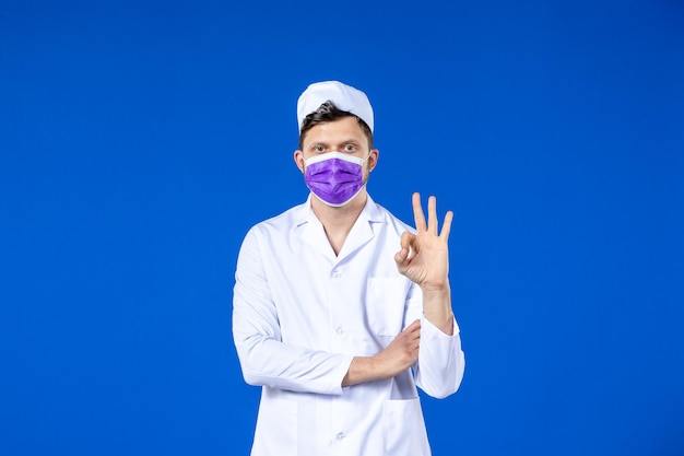 Vorderansicht des männlichen Arztes im medizinischen Anzug und in der lila Maske auf Blau