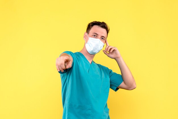 Vorderansicht des männlichen Arztes in der Schutzmaske auf gelber Wand