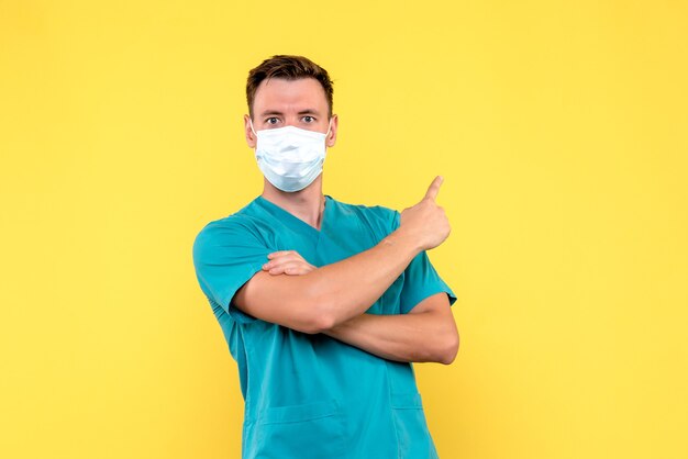 Vorderansicht des männlichen Arztes in der sterilen Maske auf gelber Wand