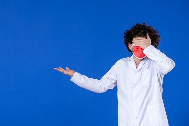 Vorderansicht des männlichen arztes in medizinischem anzug und maske auf blauem hintergrund impfstoff-kovid-gesundheitsmedizin-virus-krankenhaus-medikamentenpandemiefarbe