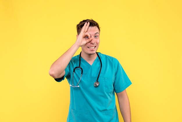 Vorderansicht des männlichen Arztes mit aufgeregtem Ausdruck auf gelbem Bodenemotionskrankenhausmediziner