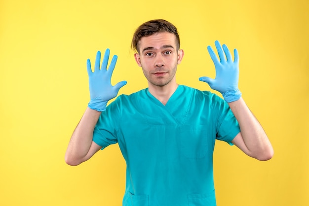 Vorderansicht des männlichen Arztes mit blauen Handschuhen auf gelber Wand