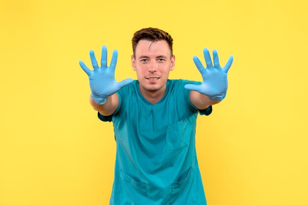 Vorderansicht des männlichen Arztes mit blauen Handschuhen auf gelber Wand