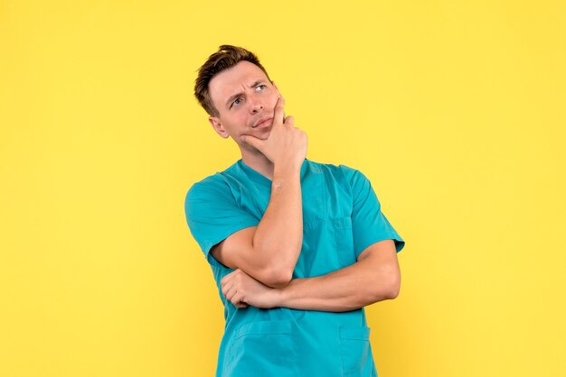 Vorderansicht des männlichen Arztes mit denkendem Ausdruck auf gelber Wand