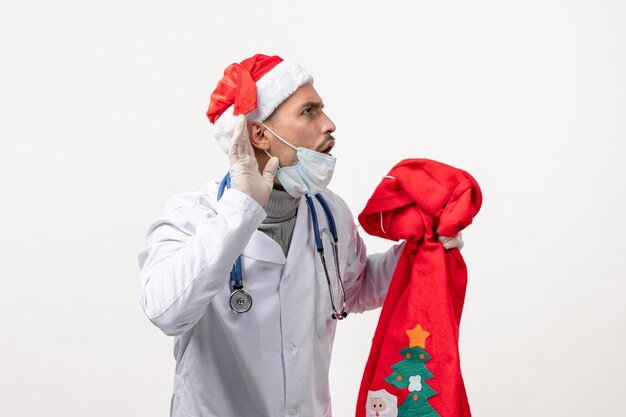 Vorderansicht des männlichen Arztes mit Geschenktüte auf weißer Wand
