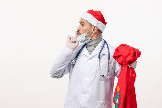 Vorderansicht des männlichen Arztes mit Geschenktüte auf weißer Wand