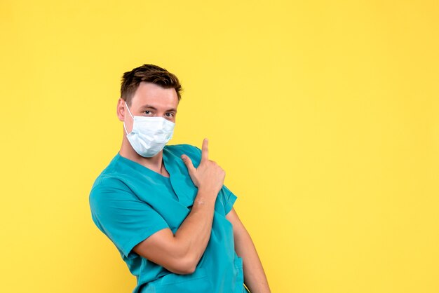 Vorderansicht des männlichen Arztes mit Maske auf gelber Wand