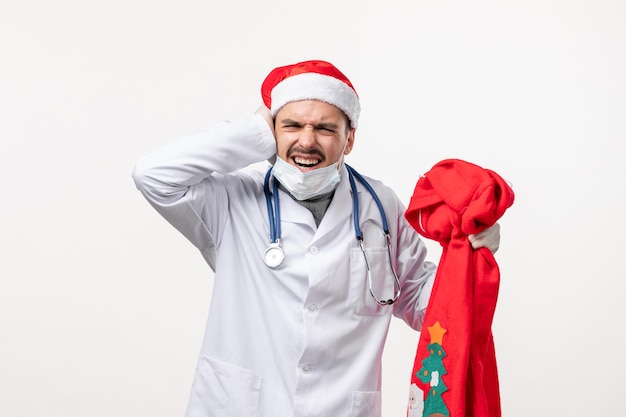 Vorderansicht des männlichen Arztes mit roter Geschenktüte auf weißer Wand