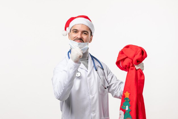 Vorderansicht des männlichen Arztes mit roter Geschenktüte auf weißer Wand