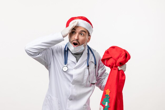 Vorderansicht des männlichen Arztes mit roter Geschenktüte auf weißer Wand