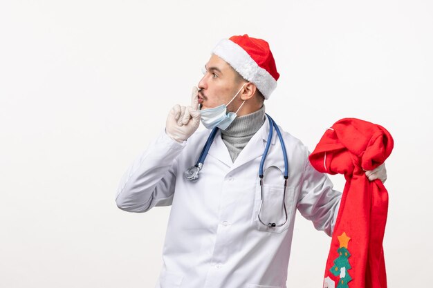 Vorderansicht des männlichen Arztes mit roter Geschenktüte auf weißer Wand