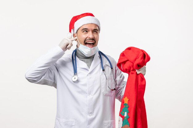 Vorderansicht des männlichen Arztes mit roter Geschenktüte auf weißer Wand