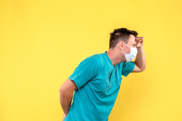 Vorderansicht des männlichen Arztes mit steriler Maske auf gelber Wand