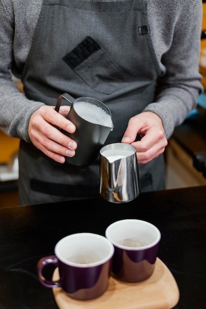 Vorderansicht des männlichen Barista, der Milchschaum in Tassen gießt