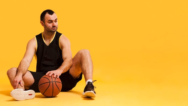 Kostenloses Foto vorderansicht des männlichen basketball-spielers, der sich mit ball- und kopienraum hinsetzt