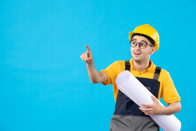 Vorderansicht des männlichen Baumeisters in der gelben Uniform mit Papierplan auf Blau