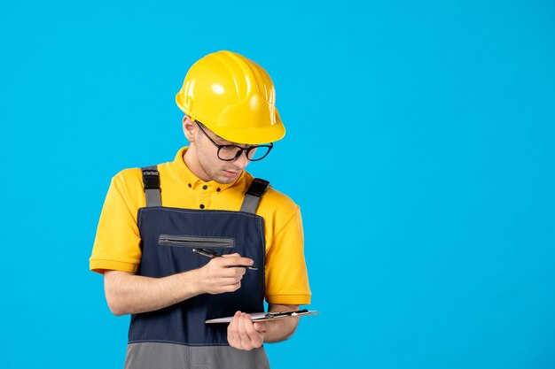 Vorderansicht des männlichen Baumeisters in der Uniform und im Helm, die Notizen auf blauer Wand machen